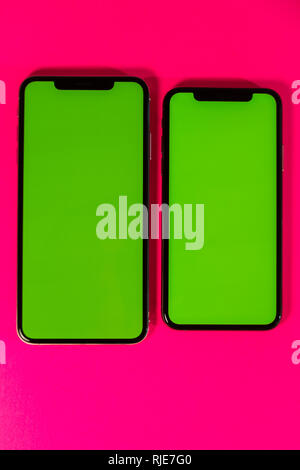 PARIS, FRANCE - SEP 27, 2018: Copy space as green chroma key on Apple Computers iPhone Xs and Xs Max as hero object on bright glamorous modern neon pop fuchsia background - smartphone telephone with OLED display Stock Photo