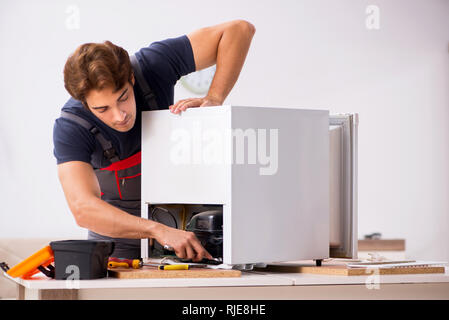Young handsome contractor repairing fridge Stock Photo