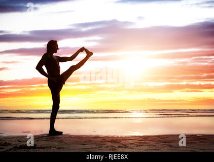 Fit Man in silhouette doing Yoga on the beach near the ocean at beautiful sunset in India Stock Photo