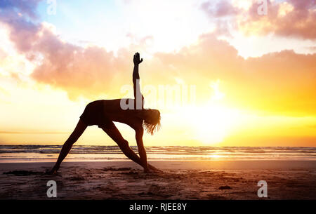 Fit Man in silhouette doing Yoga on the beach near the ocean at beautiful sunset in India Stock Photo