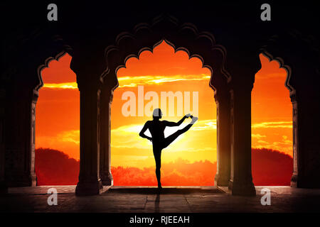 Man silhouette doing yoga advance balance asana in old temple at orange sunset sky background Stock Photo