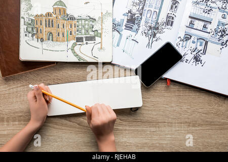 top view of womans hands holding pencil, albums with paints and smartphone on wooden background Stock Photo
