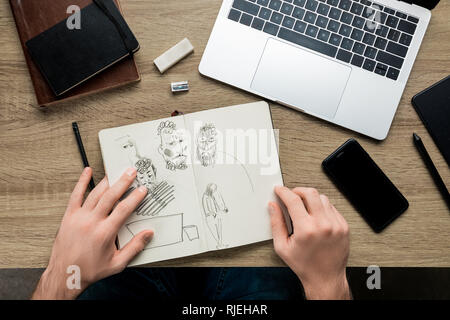 top view of mans hands laying on wooden table along album with sketches, laptop and a smartphone Stock Photo