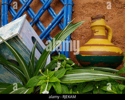 Yellow ceramic jug, blue wooden grill and green plant on brown wall background, Rabat, Morocco. Stock Photo