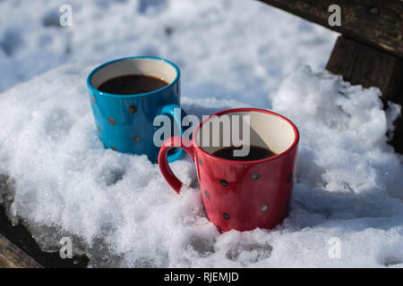 Red and blue cups with coffee on the bench in the park covered with the snow on the Kosmaj mountain Stock Photo
