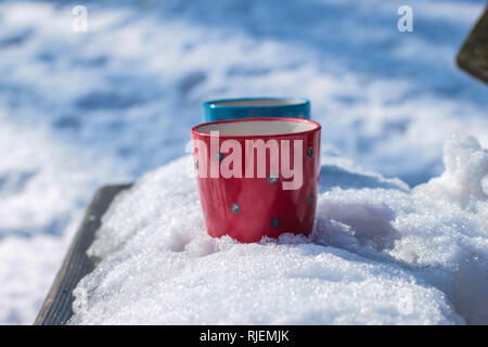 Red and blue cups with coffee on the bench in the park covered with the snow on the Kosmaj mountain Stock Photo