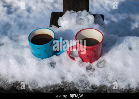 Red and blue cups with coffee on the bench in the park covered with the snow on the Kosmaj mountain Stock Photo