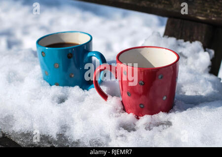 Red and blue cups with coffee on the bench in the park covered with the snow on the Kosmaj mountain Stock Photo