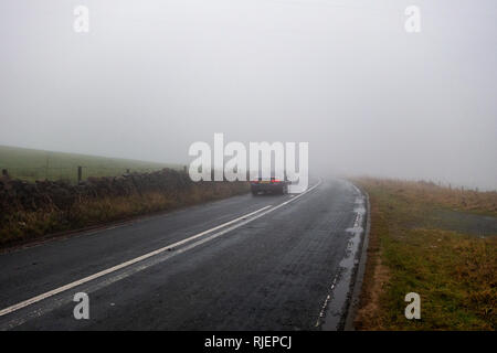 A Vehicle travelling away from camera in the Winters Low Cloud fog on the B6232 Elton Road, Oswaldtwistle, Blackburn, England Stock Photo