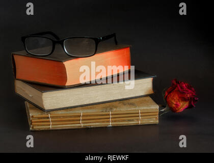 Reading glasses on top of three old books stacked on top of each other, against dark background- vintage reading concept Stock Photo