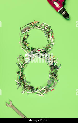 The conceptual composition from set of nails, screws and tools about Eight march womans day holiday on a green background. The number 8 in decor. Top view. The women in male occupations Stock Photo