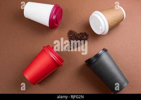 top view heart of coffee beans and various coffee drinks in paper disposable cups flat lay brown background, mock up blank paper cups Stock Photo