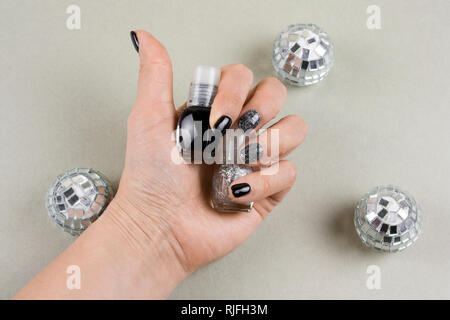 woman's hand with beautiful manicure holding nail polish bottles and disco balls top view Stock Photo