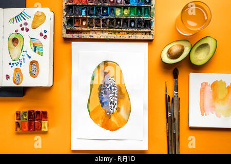 top view of papaya drawings next to colored paints and paintbrushes on yellow background Stock Photo
