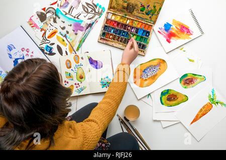 top view of woman women mixing watercolor paints while surrounded by color drawings Stock Photo