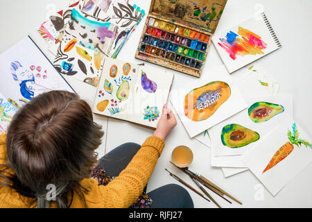 top view of sitting woman surrounded by color drawings and drawing utensils Stock Photo