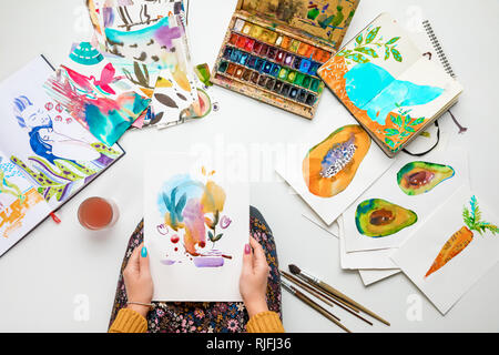 top view of woman holding watercolor drawing while surrounded by color pictures Stock Photo