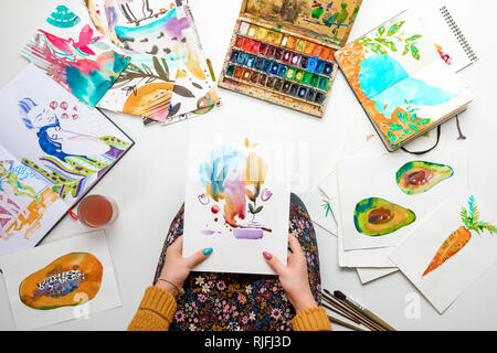 top view of woman holding watercolor drawing while surrounded by color pictures Stock Photo