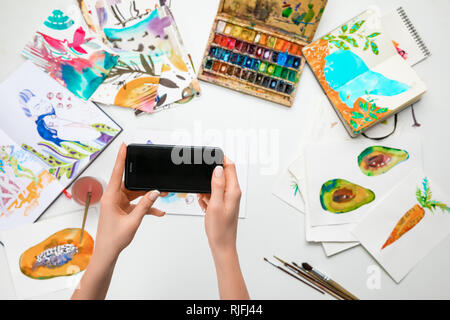 selective focus of female hands making photo of watercolor paintings and drawing utensils using smartphone Stock Photo