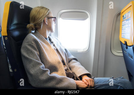 Thoughtful woman looking through the window while traveling by airplane. Stock Photo