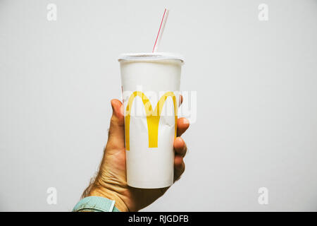 PARIS, FRANCE - JUL 27, 2018: Man holding against white background a cup of McDonald's Cola with plastic straw with yellow logo near one of the world's largest fast food restaurants Stock Photo