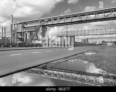 Oil refinery with scaffolds and crossing pipelines reflected in a pond against a dramatic, Port of Antwerp, Belgium Stock Photo