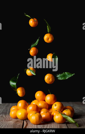 tasty orange tangerines with green leaves falling on wooden table isolated on black Stock Photo
