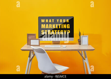 Computer with what your marketing strategy question on screen at wooden table on yellow background Stock Photo