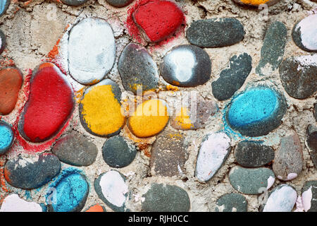 Colorful painted cobble stones on the rough textured surface of a pebble stone wall Stock Photo
