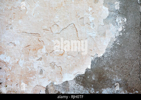 Pastel beige colored, dirty, old and cracked plastered grunge wall with peeling paint flakes on it. Background wallpaper. Stock Photo