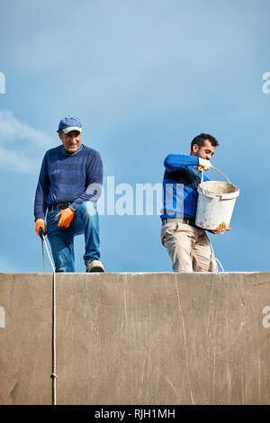 Bodrum, Turkey - January 2019: Two Turkish construction workers working at the top of a building and pulling the buckets up with ropes against a cloud Stock Photo