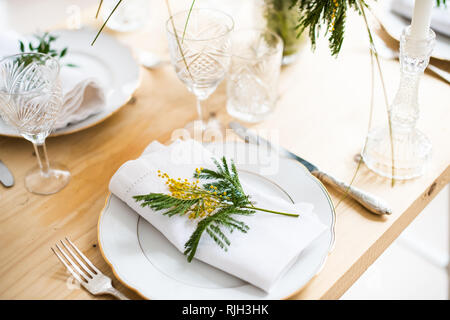 Beautiful springtime table setting with green leaves and mimosa branches, bright white table dinner decoration Stock Photo