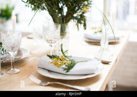 Beautiful springtime table setting with green leaves and mimosa branches, bright white table dinner decoration Stock Photo