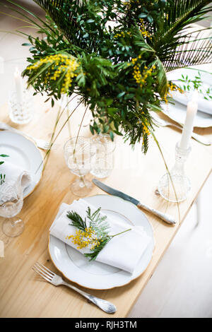 Beautiful springtime table setting with green leaves and mimosa branches, bright white table dinner decoration Stock Photo