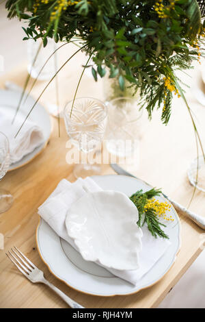 Beautiful springtime table setting with green leaves and mimosa branches, bright white table dinner decoration Stock Photo