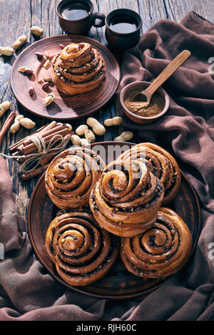 freshly baked Cinnamon rolls buns with peanuts served on a earthenware plate and two cups of coffee on an old wooden table. Kanelbulle swedish dessert Stock Photo