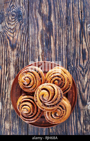 freshly baked Cinnamon rolls buns with peanuts served on a earthenware plate. Kanelbulle swedish dessert, vertical view from above,  copy space