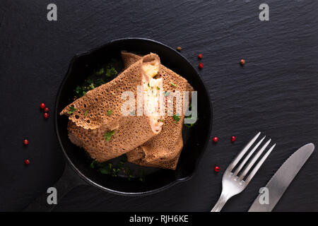 Food concept homemade Ham and Cheese Crepe in iron skillet cast on black slate background Stock Photo