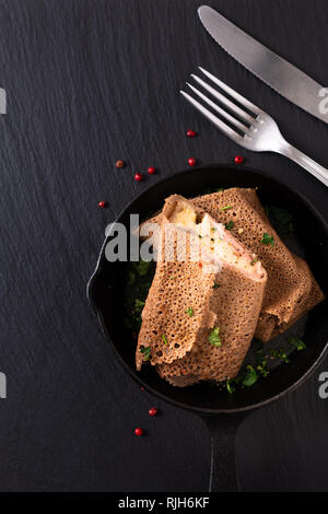 Food concept homemade Ham and Cheese Crepe in iron skillet cast on black slate background Stock Photo