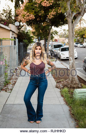 Portrait confident, tough Latinx young woman with tattoos on neighborhood sidewalk