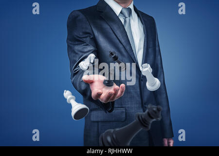 A businessman in suit standing with only upper-body visible, holding his hand out as if to reach chesspieces floating in the air. Stock Photo