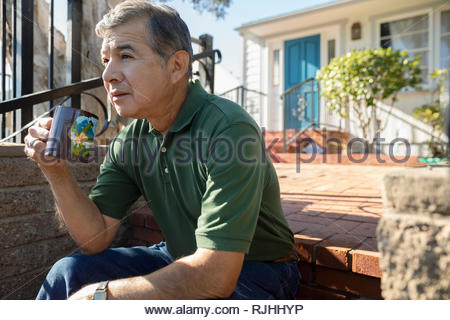 Senior Latinx man drinking coffee on sunny front stoop