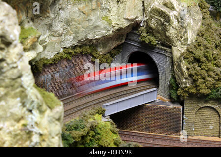 Electric Model Train on miniature train track going through mountain tunnel Stock Photo