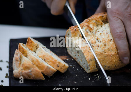 Whole grain bread put on kitchen wood plate with a chef holding gold knife for cut Stock Photo