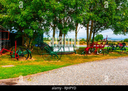 Refurbished and newly painted agricultural machinery resting on the grass among other farming tools close to the blacksmith's shop at Gretna Green Stock Photo