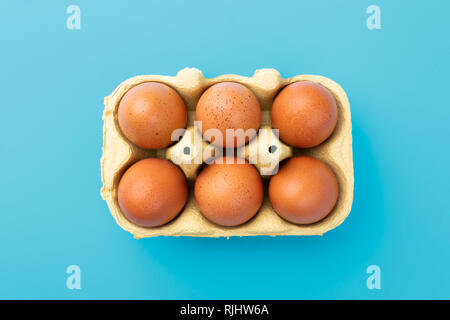 Six brwon eggs in mould box on blue turquoise background, view from above Stock Photo