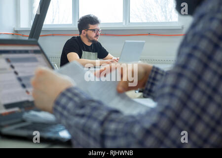 Young businessmen sitting at the desk. Business community working in open space office. Students at modern library. Business colleagues working at a b Stock Photo