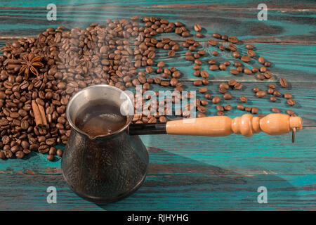 Freshly brewed coffee in cezve (jezve) and scattered roasted coffee beans, cinnamon and star anise on the turquoise wooden table Stock Photo