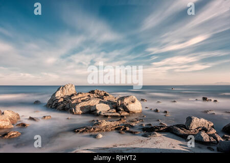 Long exposure image of Mediterranean sea washing over rocks and onto sandy beach at sunrise near Ile Rousse in Corsica Stock Photo