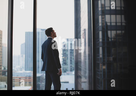 Businessman looking up at skyscraper thinking Stock Photo